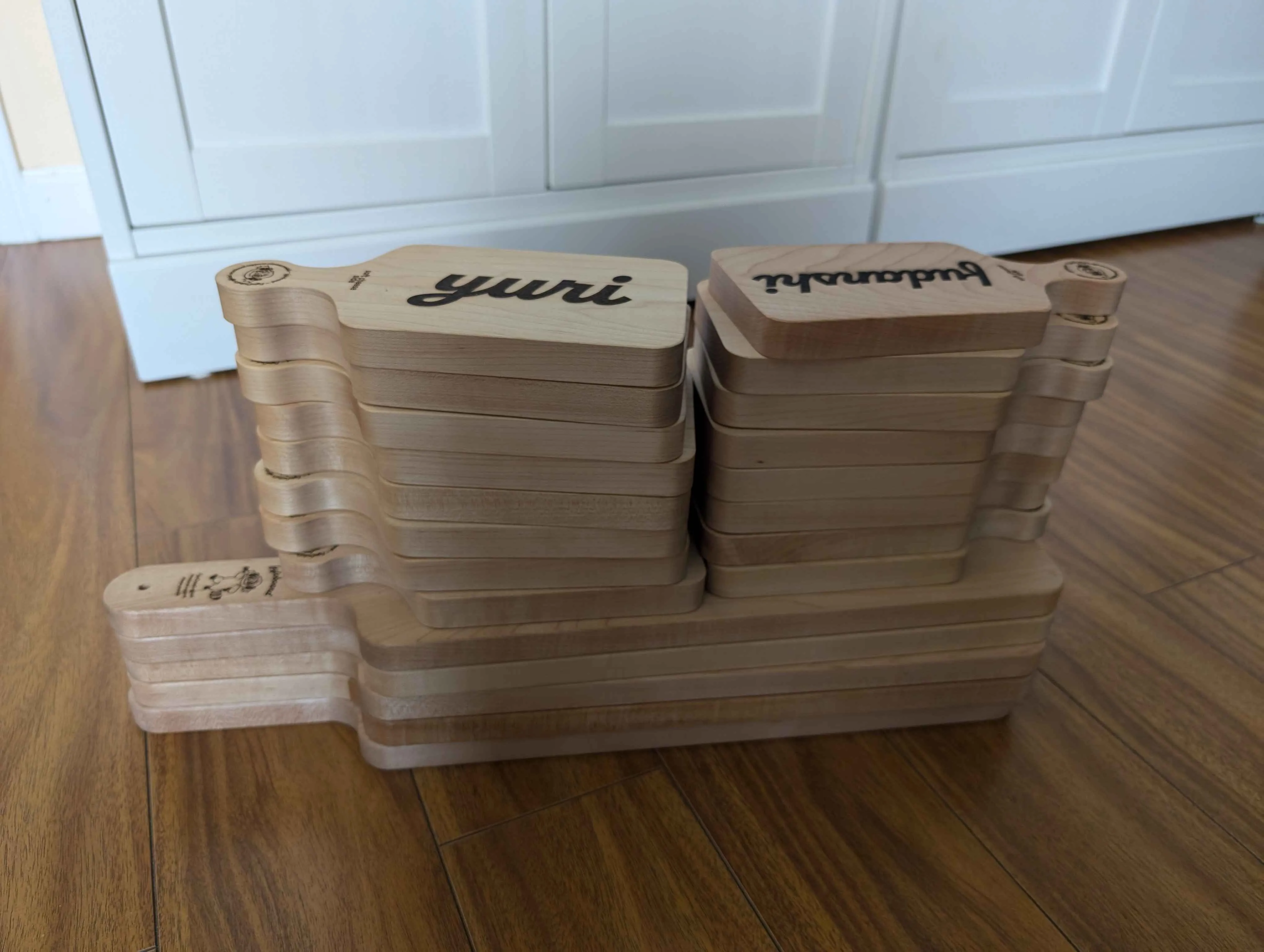 A stack of laser-cut cheese boards. The bottom of the stack is five large
“hime”-sized boards. On top of those are two stacks of eight “chibi”-sized
boards. The two visible chibi boards say Yuri and Fujoshi.