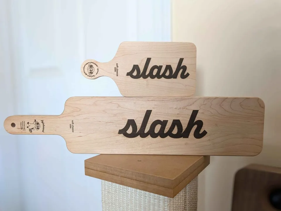 Wooden cheese boards with laser-engraved text that says ‘slash’ (as in slash
fanfiction)